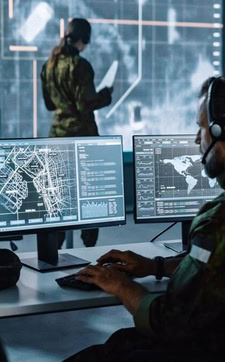 Military personnel monitoring digital maps and data on multiple screens in a high-tech control room.