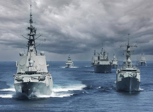Naval ships sailing in formation on the ocean under cloudy skies.