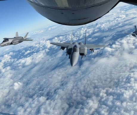 Two fighter jets flying in formation above the clouds during flight.