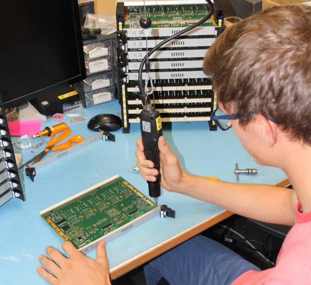 Technician repairing a circuit board with a soldering iron in a tech workshop.